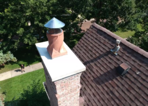 Aerial view of a chimney with a new cap on a house roof with trees in the background.