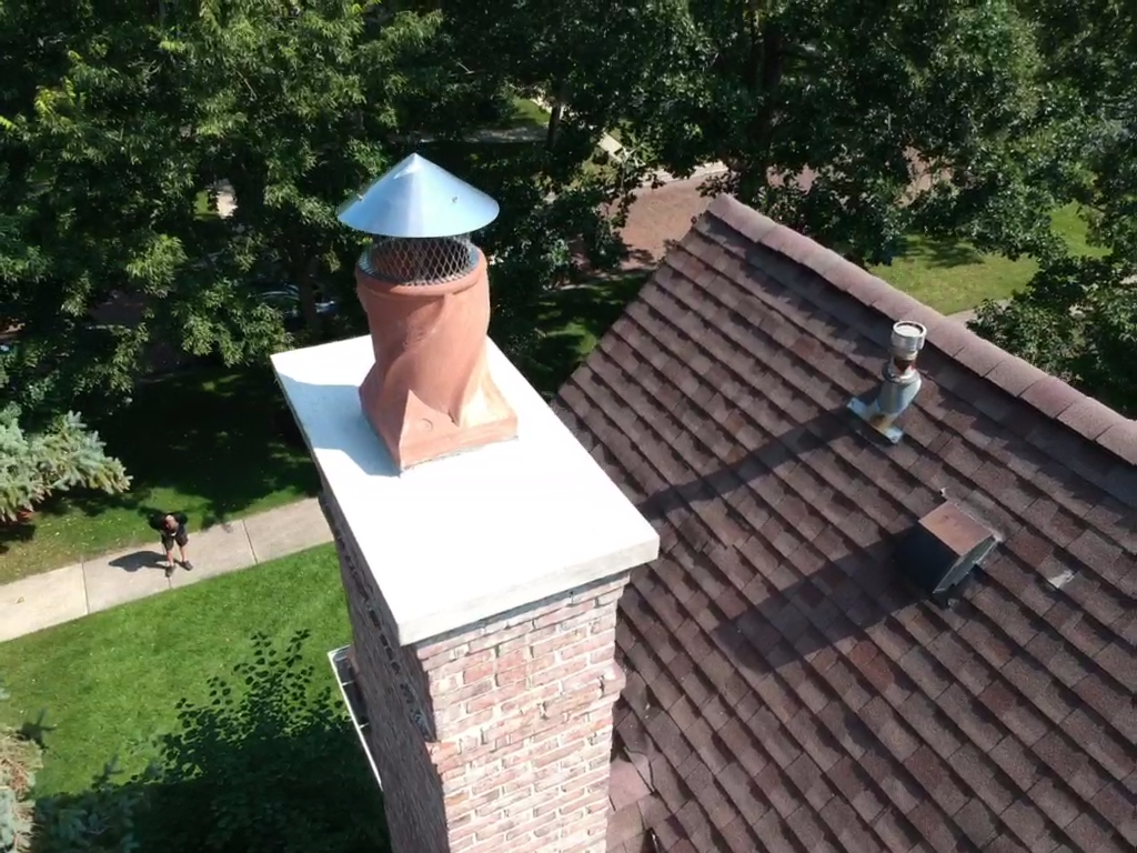 Aerial view of a chimney with a new cap on a house roof with trees in the background.