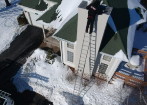 Aerial view of a technician conducting a chimney inspection service on a snowy rooftop in Lake Geneva.