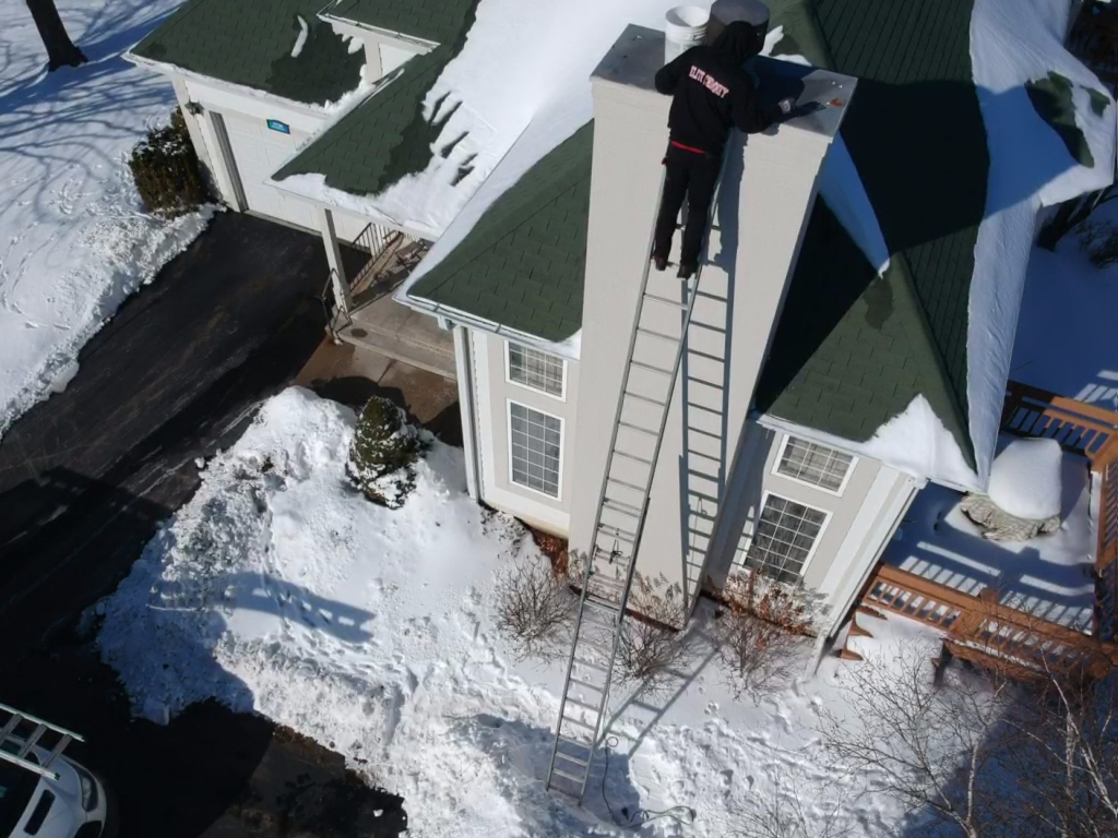 Aerial view of a technician conducting a chimney inspection service on a snowy rooftop in Lake Geneva.
